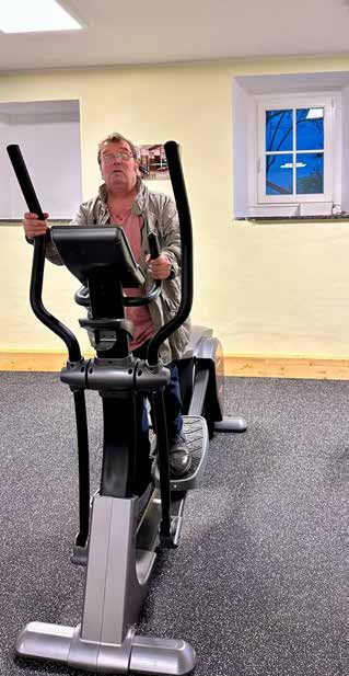 Ein Mann trainiert auf einem Crosstrainer in einem hellen Raum mit gelben Wänden und einem kleinen Fenster.