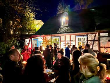 Martini-Abend: Viele Menschen stehen im Dunkeln vor einem beleuchteten Fachwerkhaus mit offenen Fenstern, einige halten Teller und Becher.