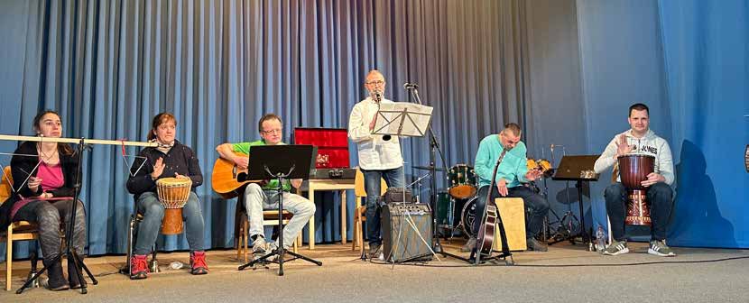 Der Instrumentalkreis spielt auf der Bühne der Festhalle mit Trommeln, Gitarren und Cajón vor einem blauen Vorhang.