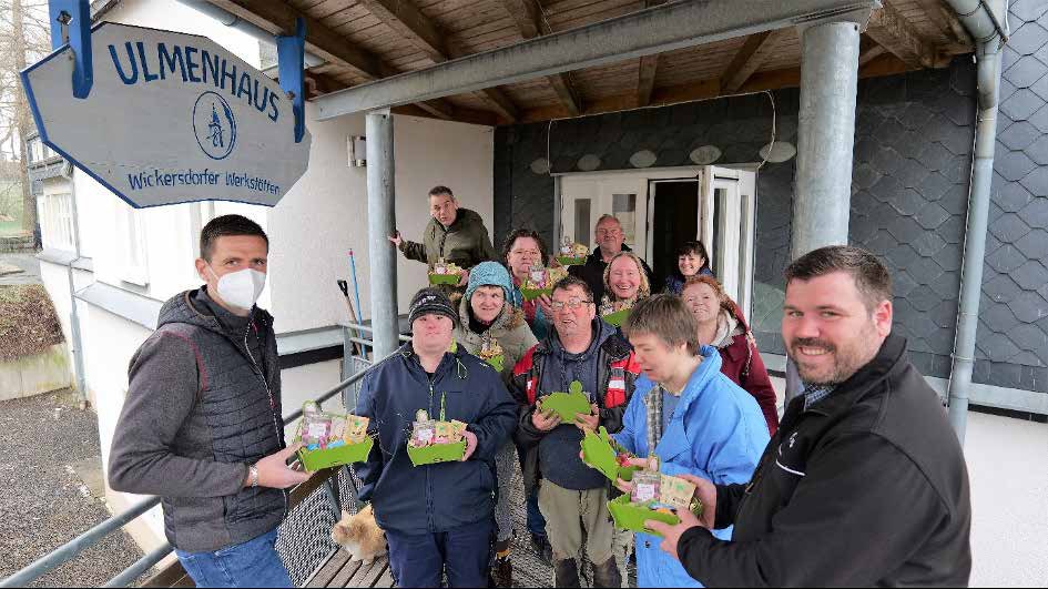 Vor dem Ulmenhaus halten Beschäftigte und Mitarbeitende kleine grüne Osternester in den Händen. Vorne stehen zwei Männer, rechts Herr Meusel, links Herr Seifert.