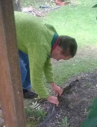 Sirko im grünen Pullover beugt sich über die Wiese und verlegt einen schwarzen Schlauch in der Erde.