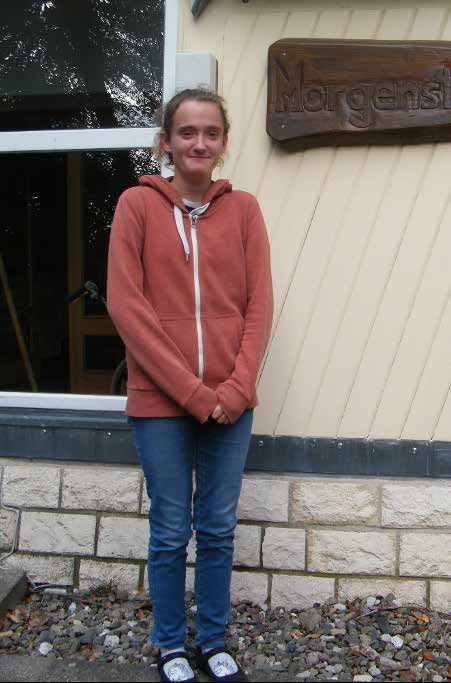 Susanne Kullack, eine junge Frau mit zurückgebundenen Haaren in einer orangefarbenen Kapuzenjacke und Jeans, steht lächelnd vor dem Morgensternhaus.