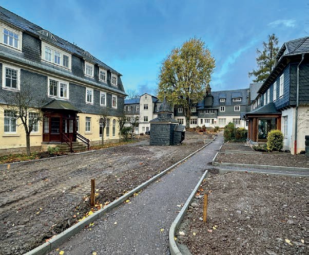 Baustelle zwischen den Häusern: ein neuer Weg mit Randsteinen führt über aufgewühlte Erde zum Türmchen in der Mitte des Platzes.