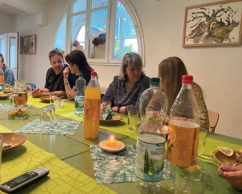 Gäste unterhalten sich an der gedeckten Tafel, auf dem Tisch ein Teelicht und Saftflaschen.