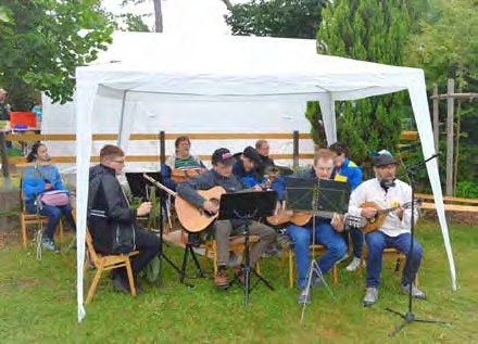 Der Instrumentalkreis spielt im Freien unter einem weißen Pavillon mit Gitarren, Mandoline und Notenständern.