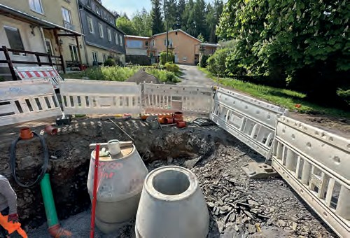 Vorher: eine aufgerissene Baustelle zwischen den Häusern, abgesperrt mit weißen Baken, in der Grube Betonschächte und Rohre.