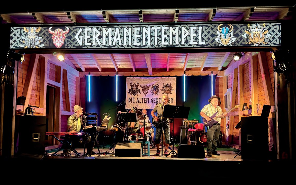 Abendliche Freiluftbühne mit dem leuchtenden Schriftzug „Germanentempel“. Eine Band spielt im bunten Scheinwerferlicht, hinten hängt ein Banner „Die Alten Germanen“.