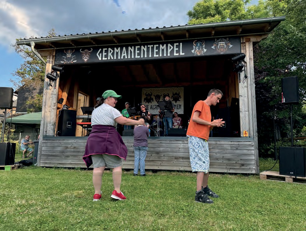 Zwei Menschen tanzen auf der Wiese vor der Bühne „Germanentempel“, auf der eine Band am Nachmittag spielt.