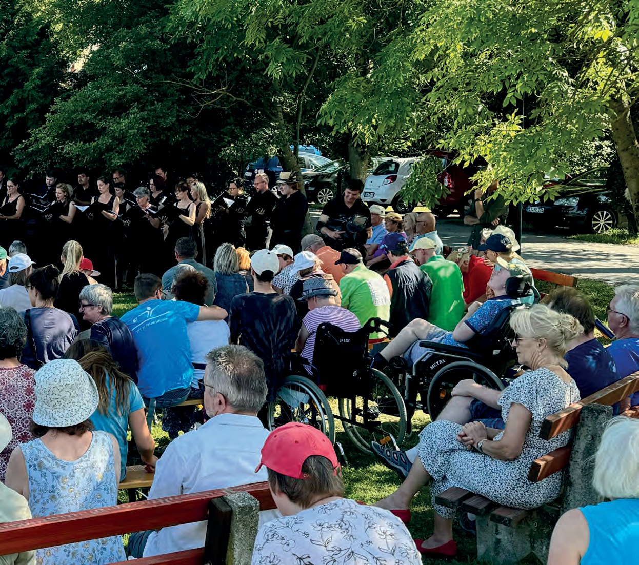 Der MDR-Rundfunkchor in schwarzer Kleidung singt unter Bäumen auf der Festwiese. Davor sitzt ein großes Publikum auf Bänken und in Rollstühlen, viele mit Sonnenhüten.