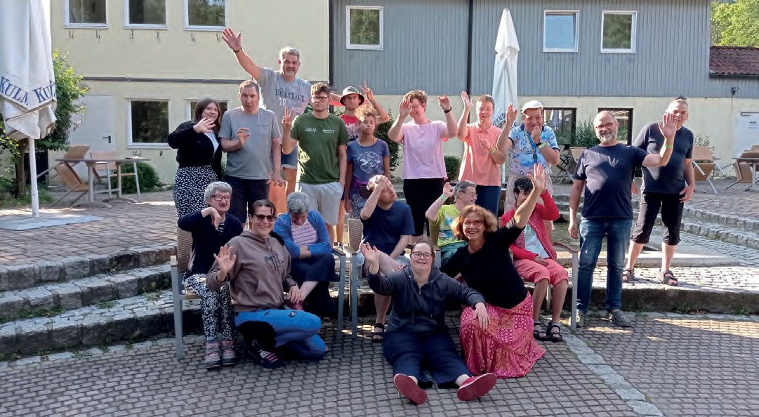 Die Urlaubsgruppe vor dem Hotel: Etwa zwanzig Bewohnerinnen, Bewohner und Mitarbeitende stehen und sitzen auf Stufen, viele winken fröhlich in die Kamera.